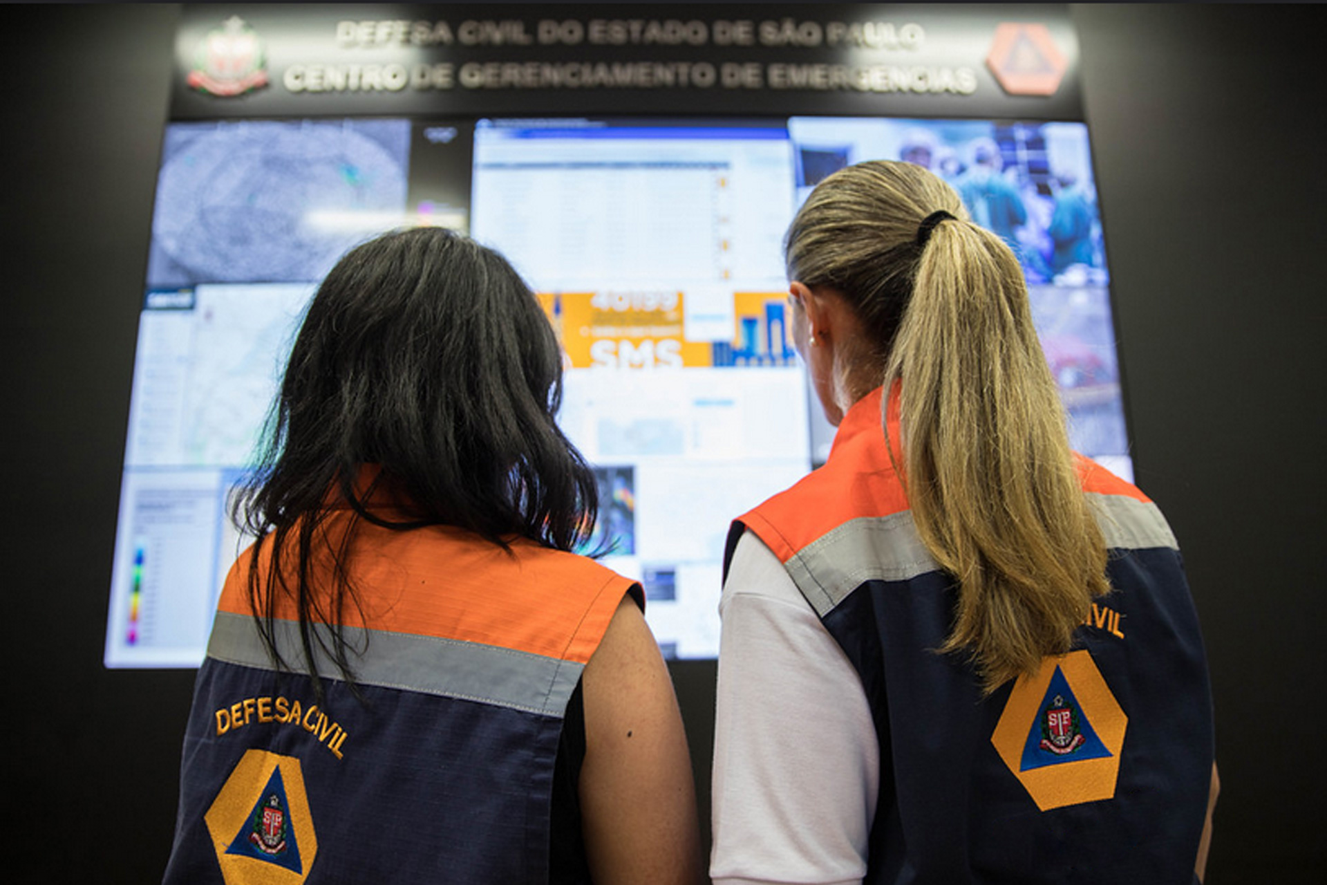 Duas mulheres da defesa civil analisando painel do centro de gerenciamento de emergências